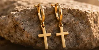 Goldfarbene Creolen mit Kreuzanhängern auf einem Stein – Symbolmotiv