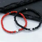 Rotes und schwarzes Perlen-Kreuzarmband auf dunklem Stein