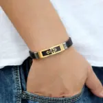Goldfarbenes Kreuzarmband mit schwarzem Silikonband am Handgelenk