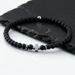 Schwarzes feines Perlenarmband mit hellem Kreuz auf Schiefer