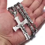Großes silberfarbenes Kruzifix mit spanischer Gebetsgravur und Königskette auf einer Hand als Größenvergleich