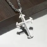 Polierter 316L-Edelstahl-Kreuzanhänger mit markanten Kreuzenden an silberfarbener Gliederkette vor dunklem Holz