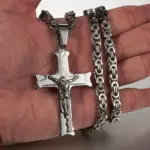 Jesus-Kruzifix mit silberfarbener Gliederkette als Größenvergleich in einer Hand