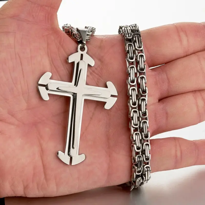 Silberner Granny Chic Kreuzanhänger neben breiter Gliederkette auf einer Hand als Größenvergleich
