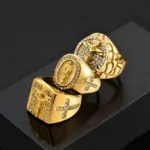 Drei PRJEWEL Jesus-Siegelring-Designs in goldfarbener Optik mit kleinen hellen Strasssteinen auf schwarzem Hintergrund