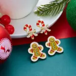 Festliche Lebkuchenmann- und Zuckerstangen-Ohrstecker auf weihnachtlicher Unterlage, Original-Lieferantenfoto