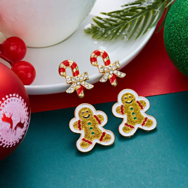 Festliche Lebkuchenmann- und Zuckerstangen-Ohrstecker auf weihnachtlicher Unterlage, Original-Lieferantenfoto