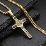 Goldfarbene Benediktus-Kreuzkette von YILUOCD mit farbigen Steinakzenten und 60 cm Kette auf dunkler Steinfläche