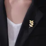 Goldfarbener Olivenzweig-Anstecker als Pflanzenmotiv an schwarzem Blazer