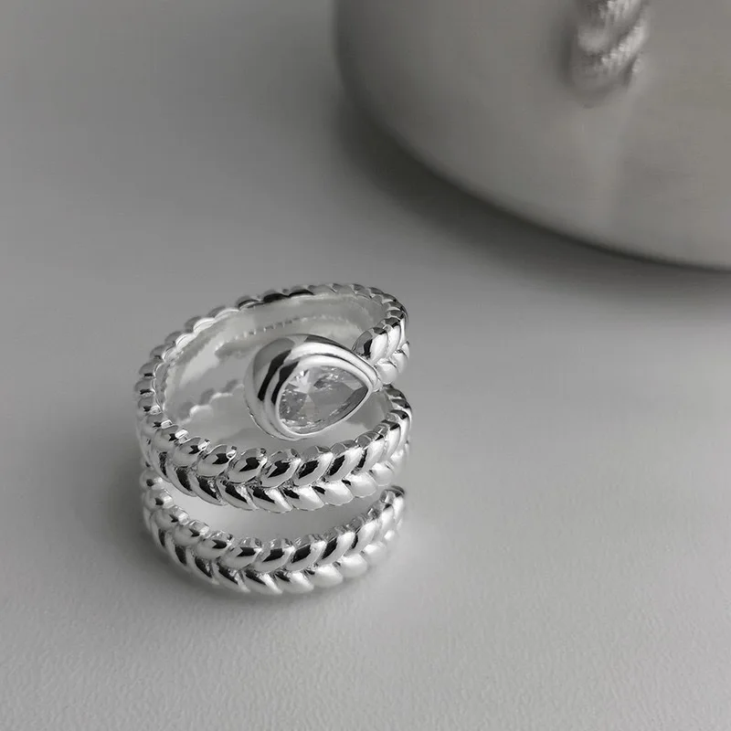 Offener BFCLUB Ring mit klarem Tropfenstein und silberfarbener gedrehter Ringschiene vor grauem Hintergrund