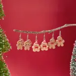 Drei Paar Lebkuchen-Ohrringe mit verschiedenen Schleifen und Mützen an einem Ast vor rotem Hintergrund