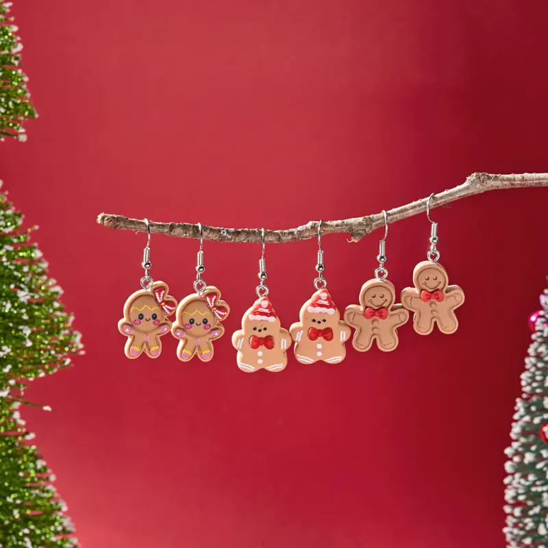 Drei Paar Lebkuchen-Ohrringe mit verschiedenen Schleifen und Mützen an einem Ast vor rotem Hintergrund