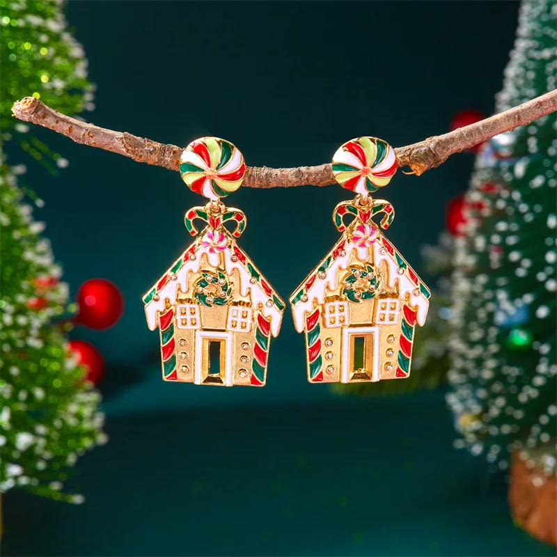 Ein Paar Lebkuchenhaus-Ohrringe mit goldfarbenen Details hängt an einem Zweig vor Weihnachtsdeko