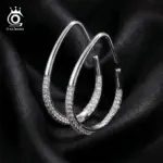 ORSA JEWELS offene tropfenförmige Creolen in Silberoptik mit hellem Steinbesatz auf schwarzem Stoff