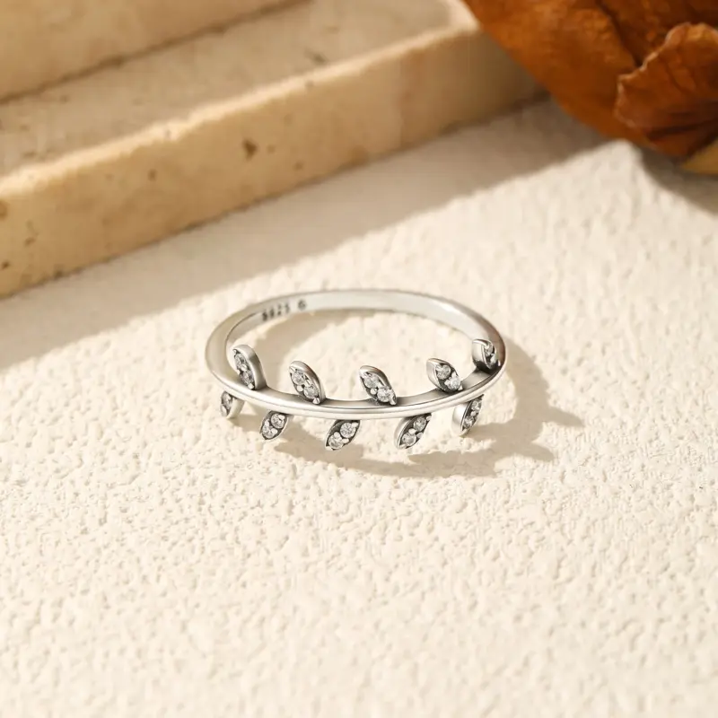 MODIAN Olivenblatt-Ring mit klaren Steinen von oben auf heller Steinoberfläche