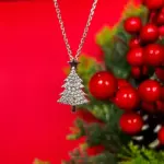 Silberfarbene Weihnachtsbaum-Halskette mit Zirkonia vor roten Beeren und Tannengrün