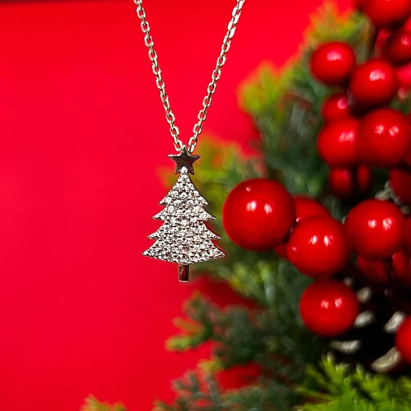 Silberfarbene Weihnachtsbaum-Halskette mit Zirkonia vor roten Beeren und Tannengrün