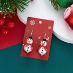 Ein Paar Schneemann-Weihnachts-Ohrhänger mit rotem Schal auf einer roten Schmuckkarte