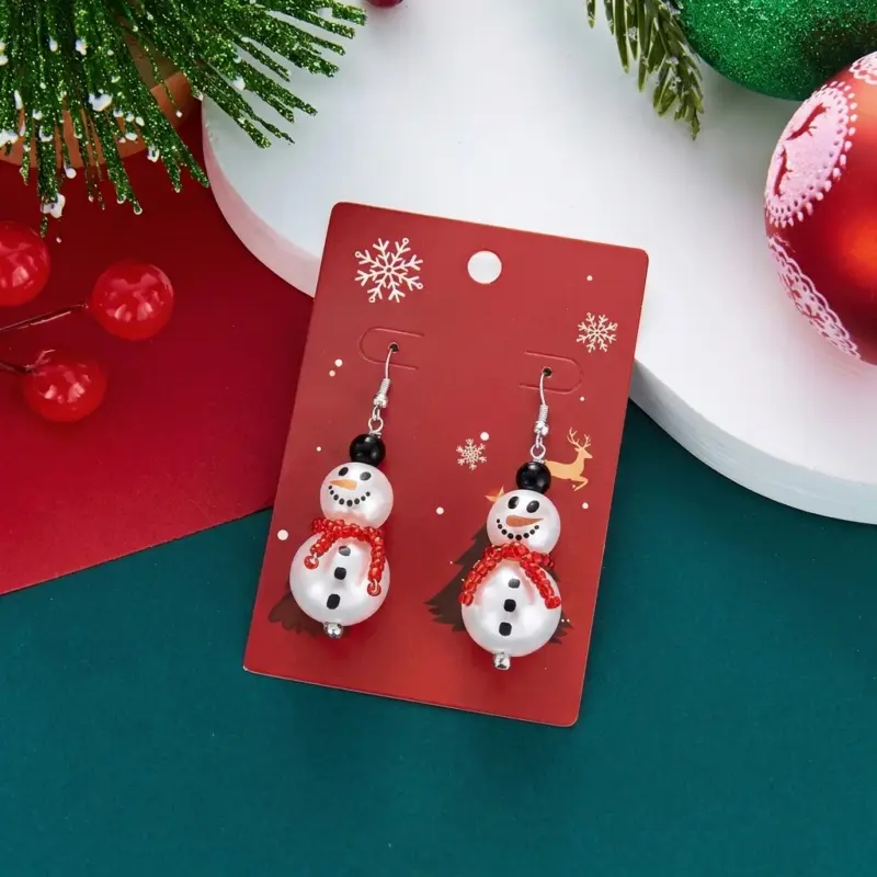 Ein Paar Schneemann-Weihnachts-Ohrhänger mit rotem Schal auf einer roten Schmuckkarte