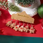 Drei Paar Lebkuchenmann-Ohrhänger mit rosa Schleife, Weihnachtsmütze und roten Fliegen vor roten Dekorationen