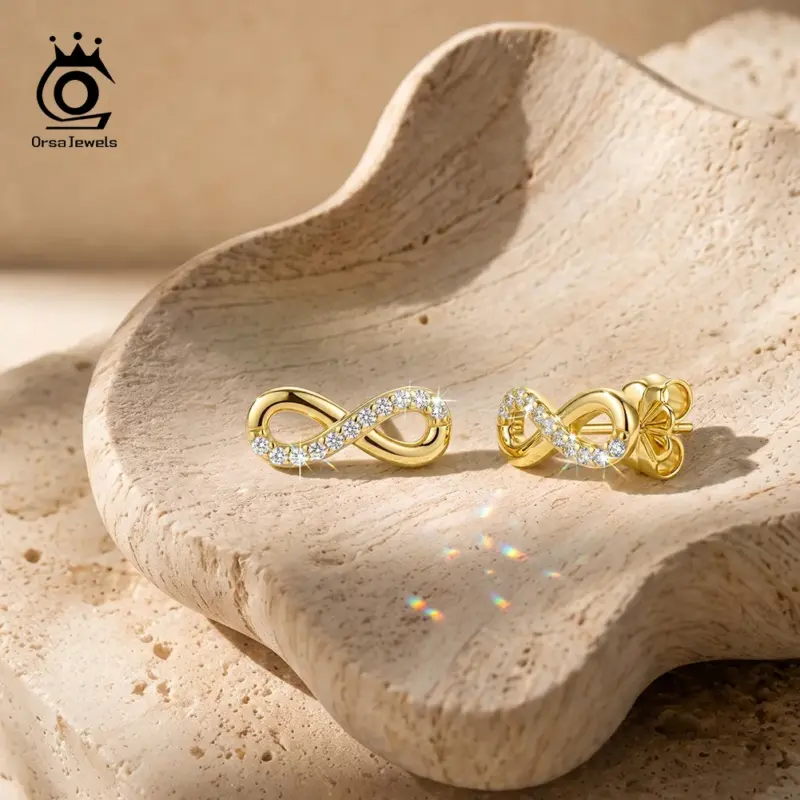 kf-Sb874f6b2c5f14e6599b6eda97c4a9874Z ORSA JEWELS goldfarbene Moissanit Unendlichkeits-Ohrstecker als Paar auf hellem Stein