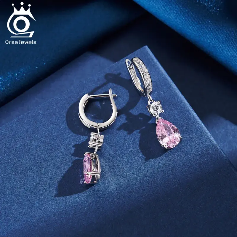 ORSA JEWELS Ohrhänger mit rosa tropfenförmigem Schmuckstein und klaren Zirkonia-Akzenten, Detailaufnahme auf blauem Stoff
