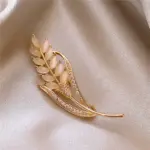 Goldfarbene Weizenähren-Brosche mit hellen ovalen Schmuckeinlagen auf grauem Satin