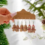 Drei Paar Lebkuchenmann-Ohrhänger mit Fliegen, bunten Knöpfen und roten Mützen auf brauner Schmuckkarte