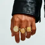 Drei goldfarbene PRJEWEL Jesus- und Kreuz-Siegelringe an einer Hand, verschiedene Motive und Formen