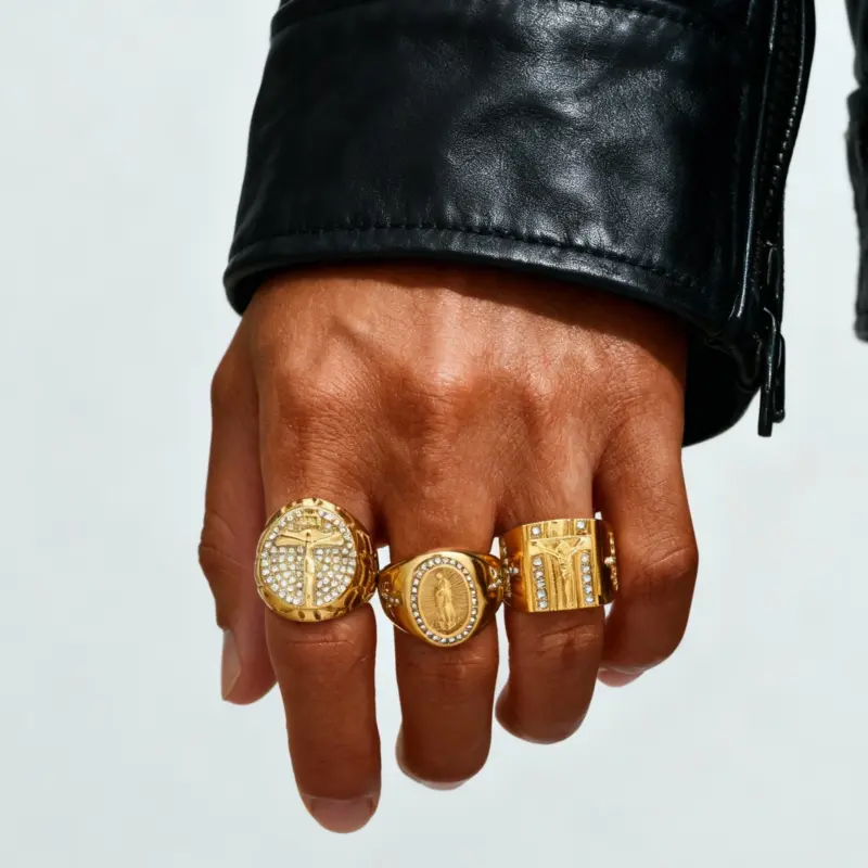 Drei goldfarbene PRJEWEL Jesus- und Kreuz-Siegelringe an einer Hand, verschiedene Motive und Formen