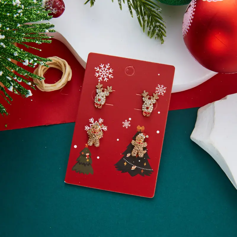 Rentierkopf und glitzernde Lebkuchenfigur als Weihnachtsohrstecker auf roter Motivkarte