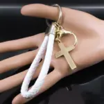 AFAWA Kreuz-Schlüsselanhänger mit JESUS-Schriftzug, weißem PU-Band und goldfarbenen Beschlägen als Größenbeispiel