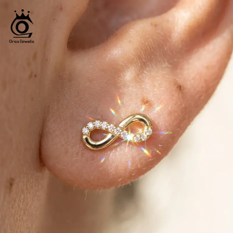 ORSA JEWELS Unendlichkeits-Ohrstecker in Goldoptik mit Moissanit am Ohr getragen